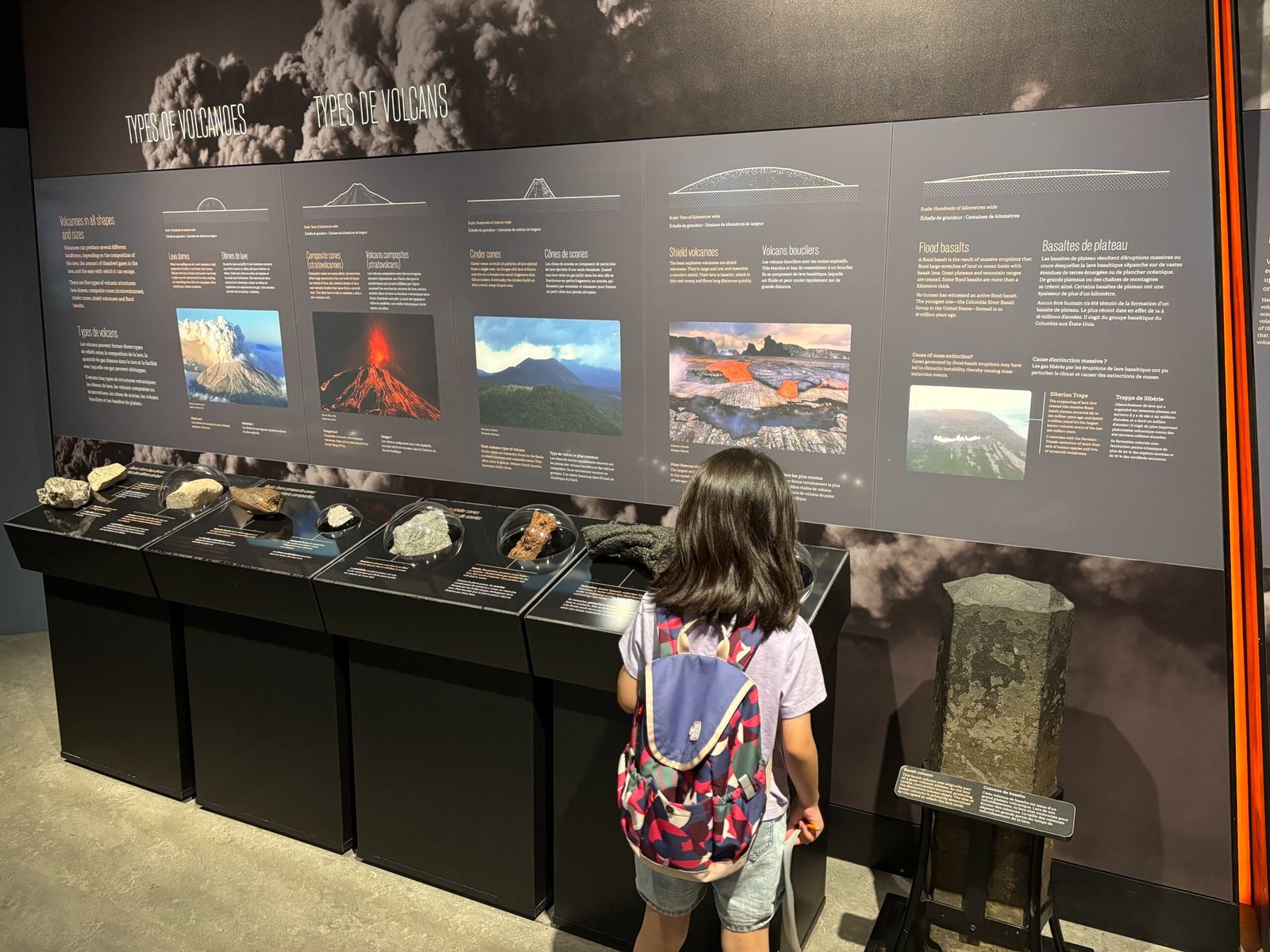 Child observing volcano types and rock samples in a museum exhibit