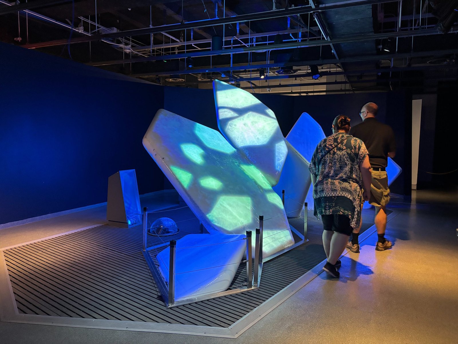 Visitors interact with a glowing iceberg sculpture in a darkened gallery