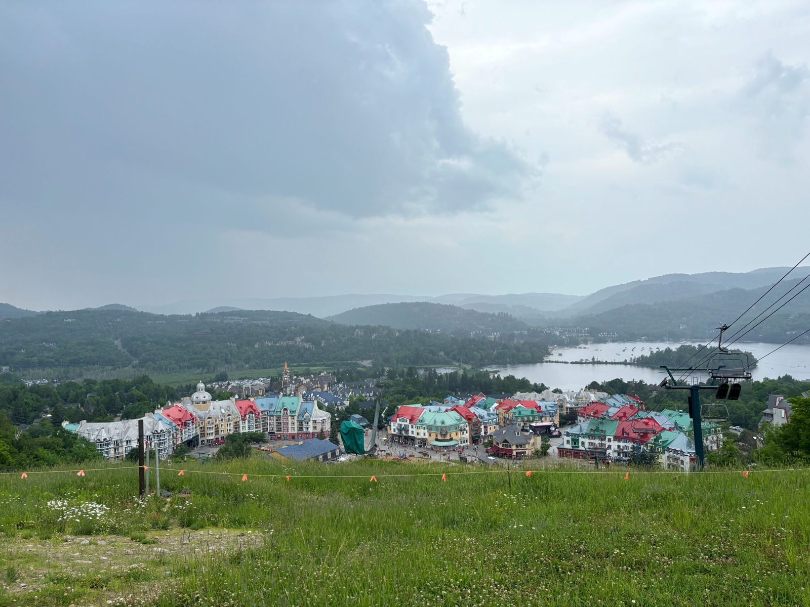 Elevated view of Mont-Tremblant village with colorful rooftops, lake in the background, and surrounding forested mountains.