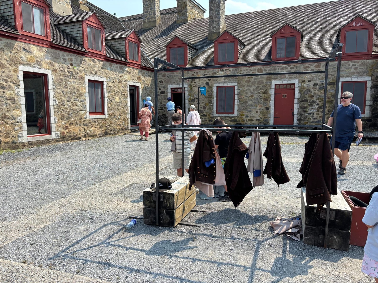 Visitors at Fort de Chambly courtyard with historic soldiers’ coats on racks for display.