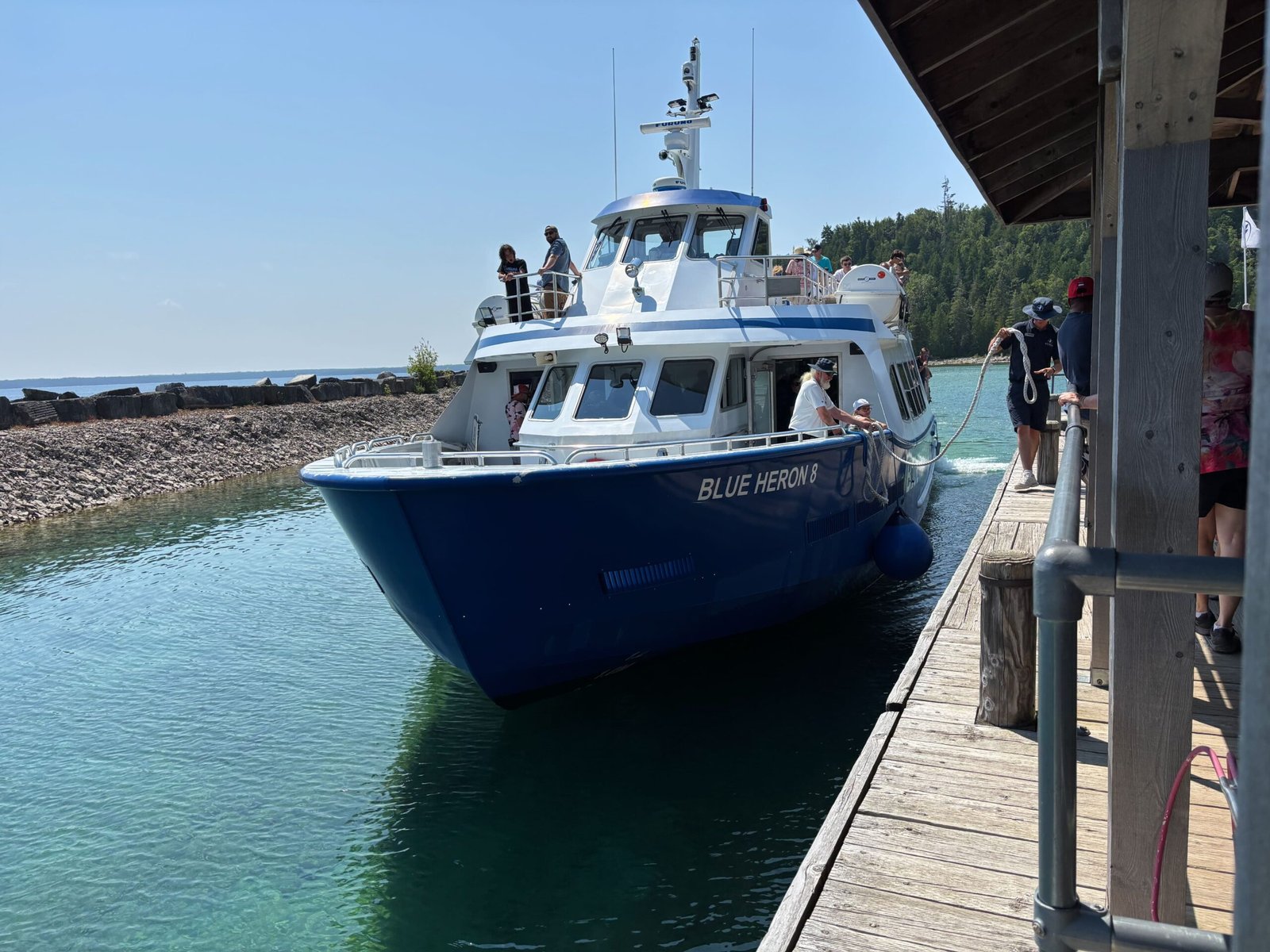 Blue Heron 8 boat docking at the pier with crew and passengers on board, surrounded by clear blue water.