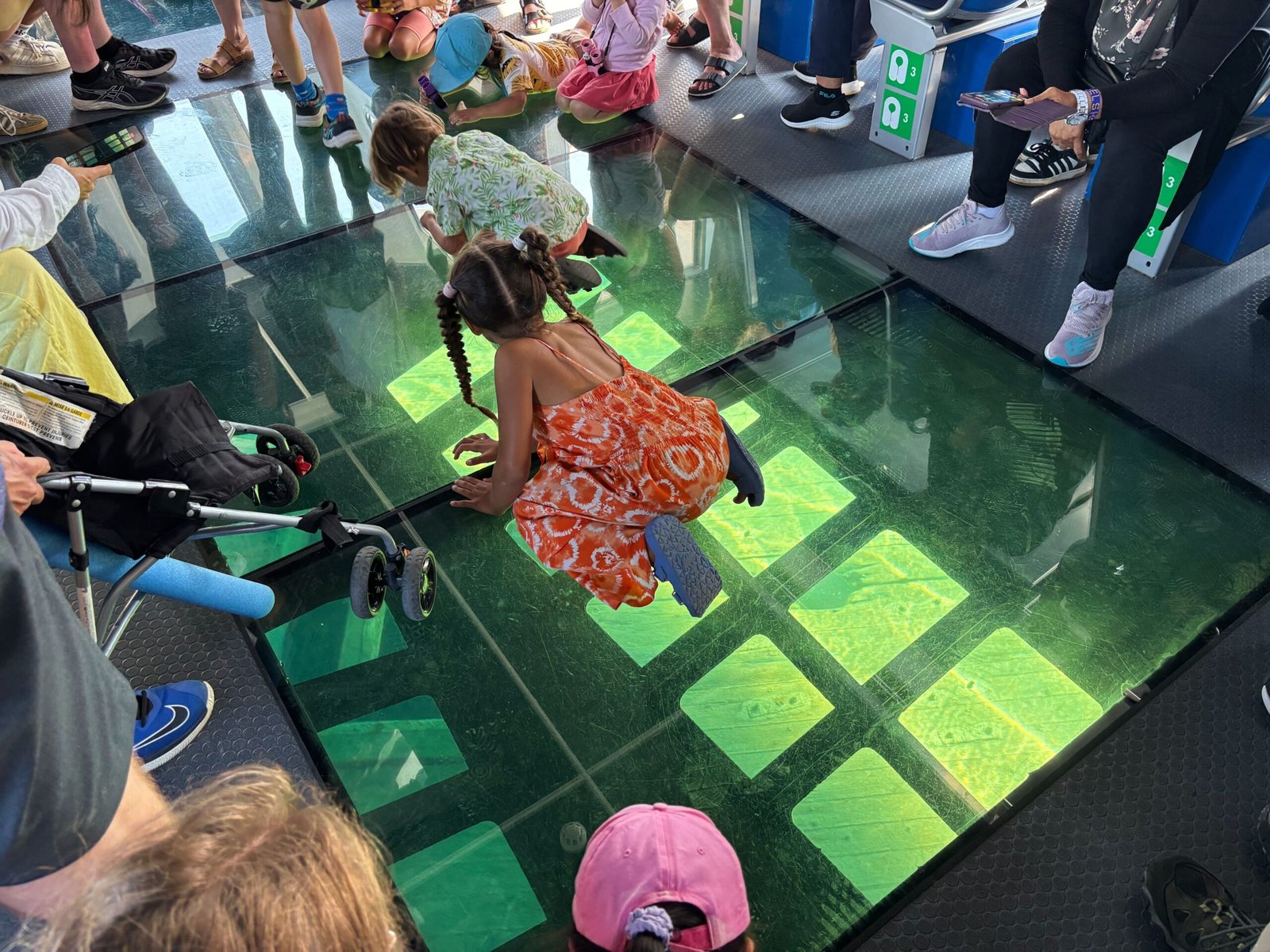 Children kneeling on the glass-bottom floor of the Blue Heron boat, looking down into the clear waters below.