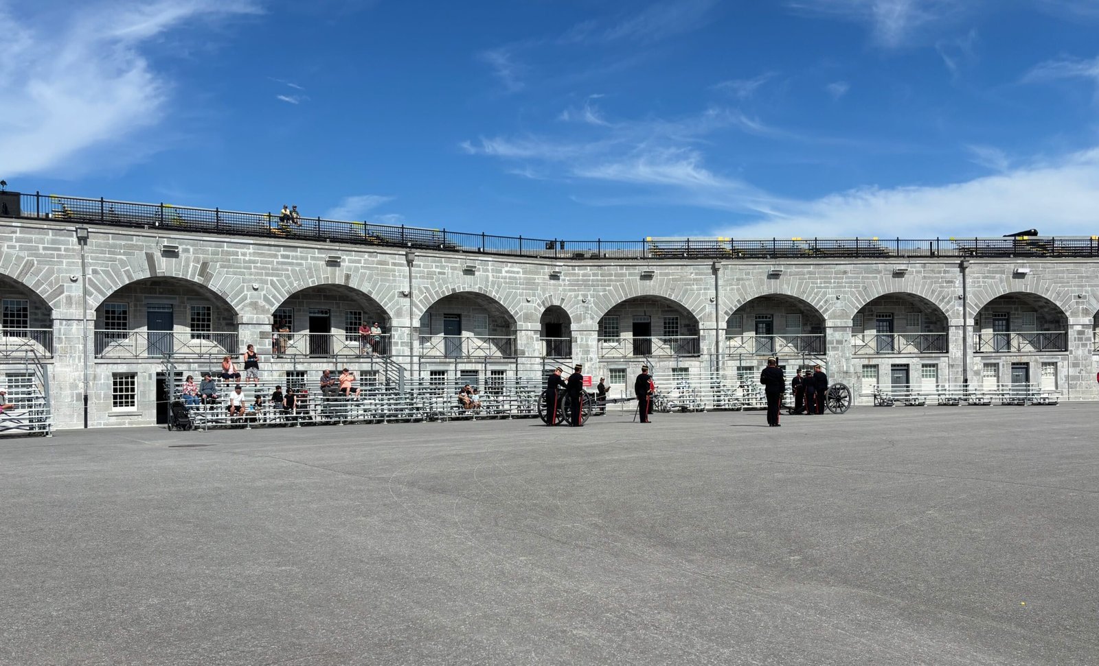 Soldiers in uniform preparing for a demonstration in Fort Henry’s parade square with spectators seated.