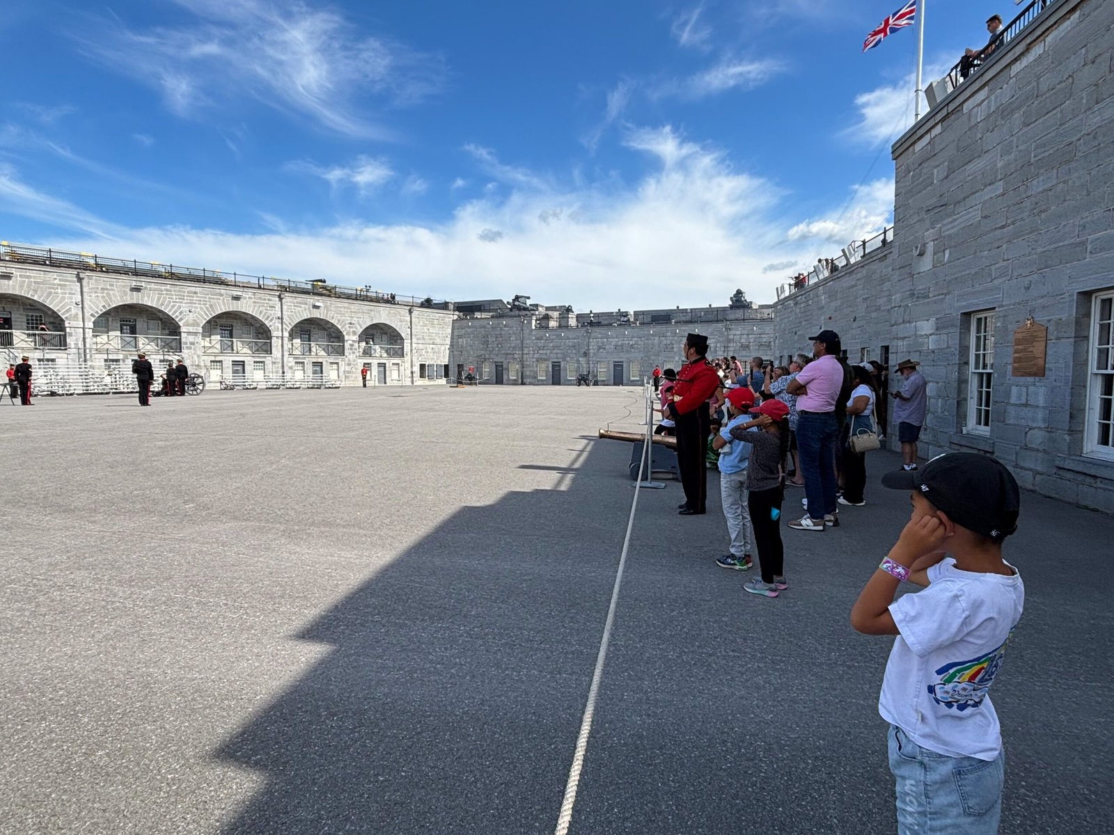 Visitors and children watching soldiers in red uniforms inside Fort Henry’s courtyard.