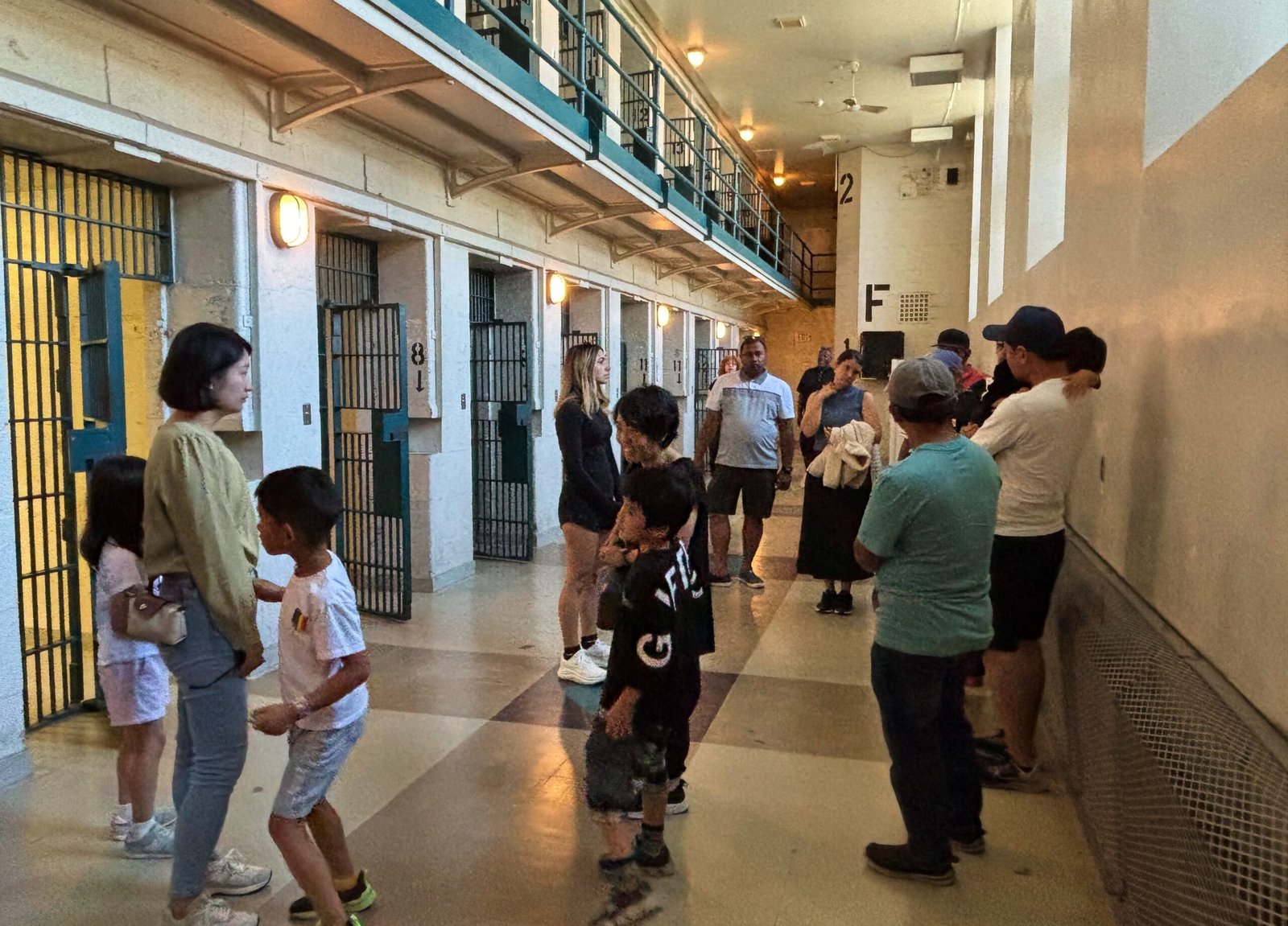Tour group standing in a prison cell block corridor with barred doors and two levels.