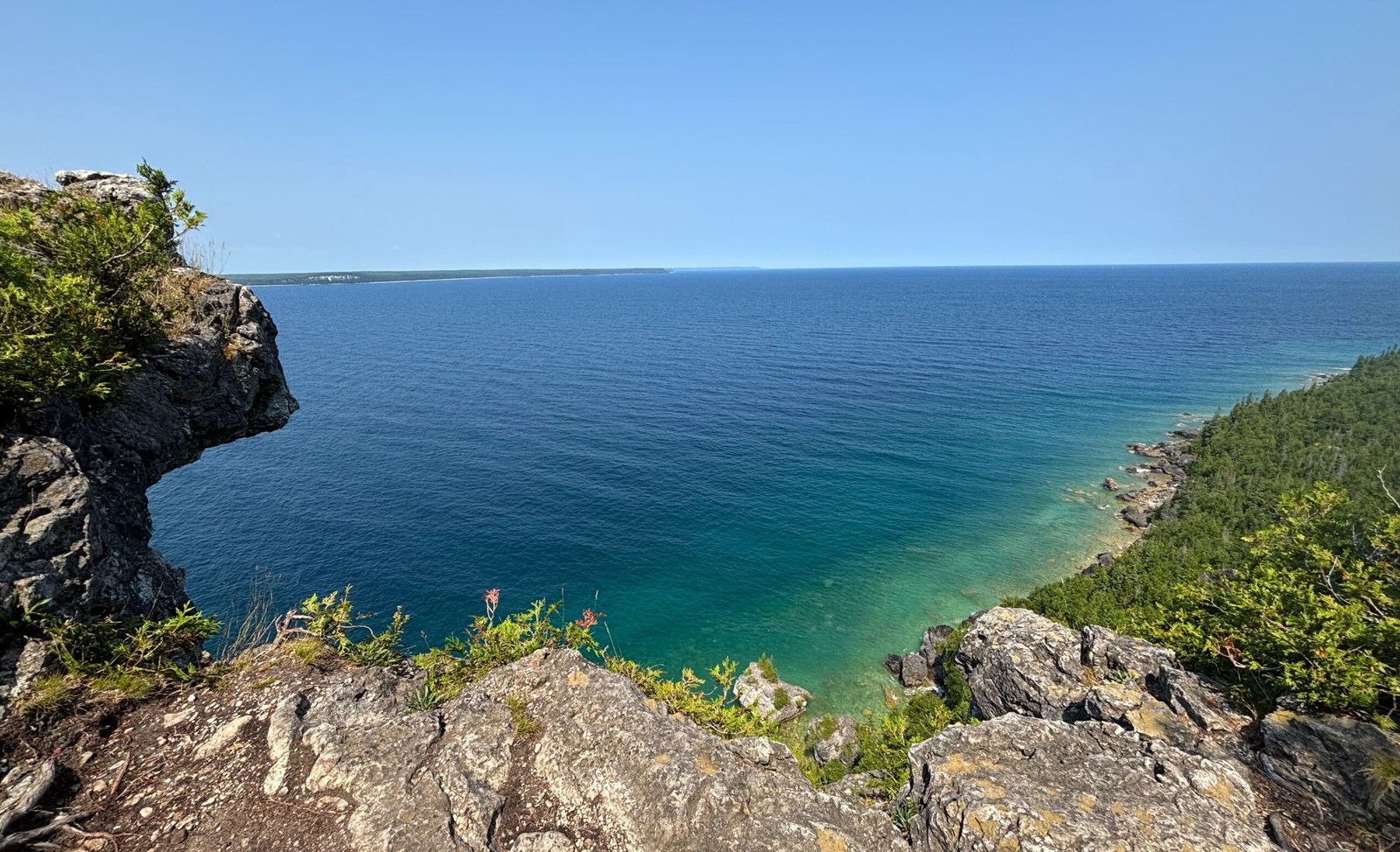 Rocky cliff edge overlooking the deep blue waters of Georgian Bay, with a sweeping view of the shoreline below.