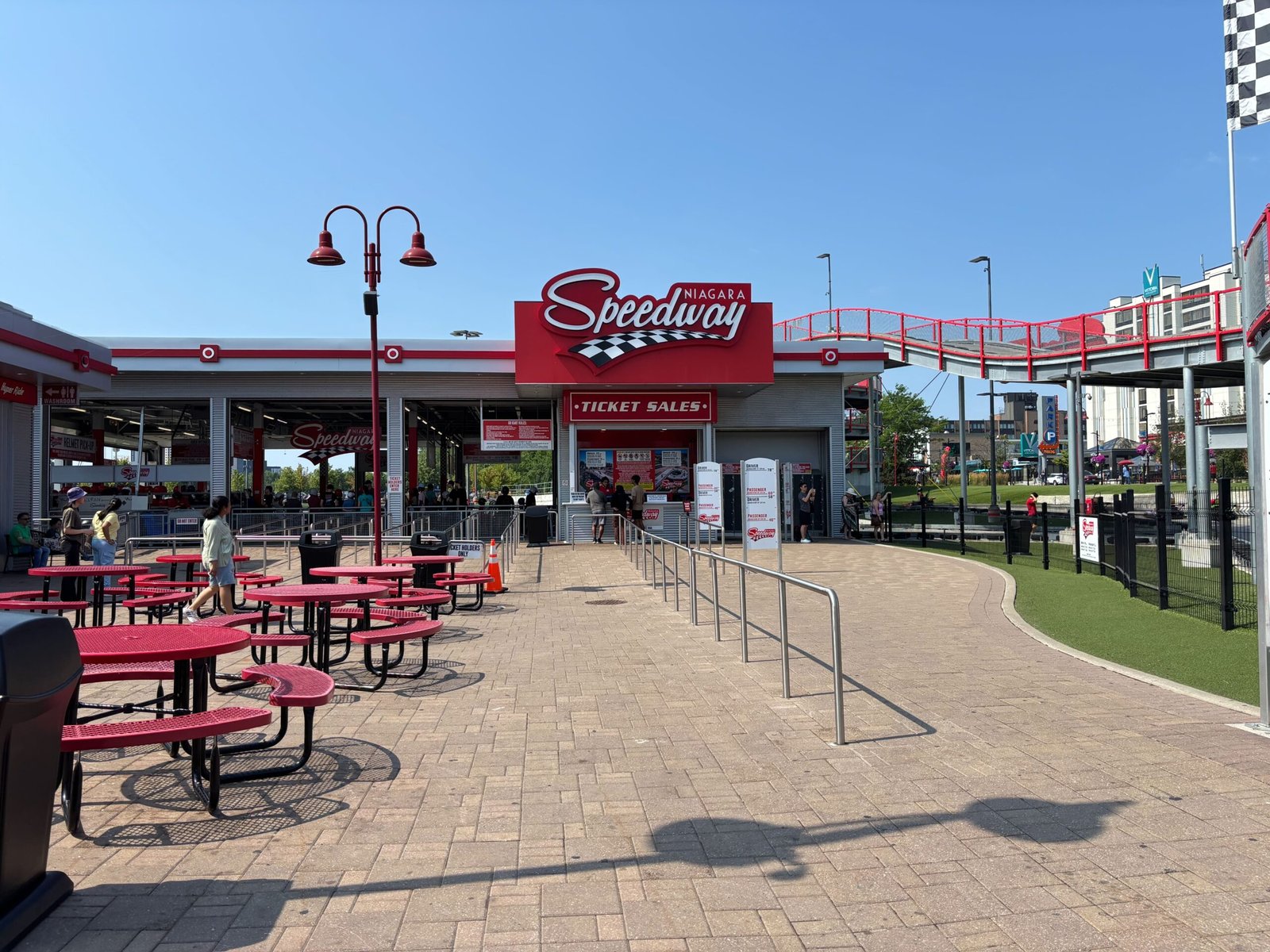 Exterior view of Niagara Speedway with ticket sales booth, red picnic tables, and elevated track in the background.