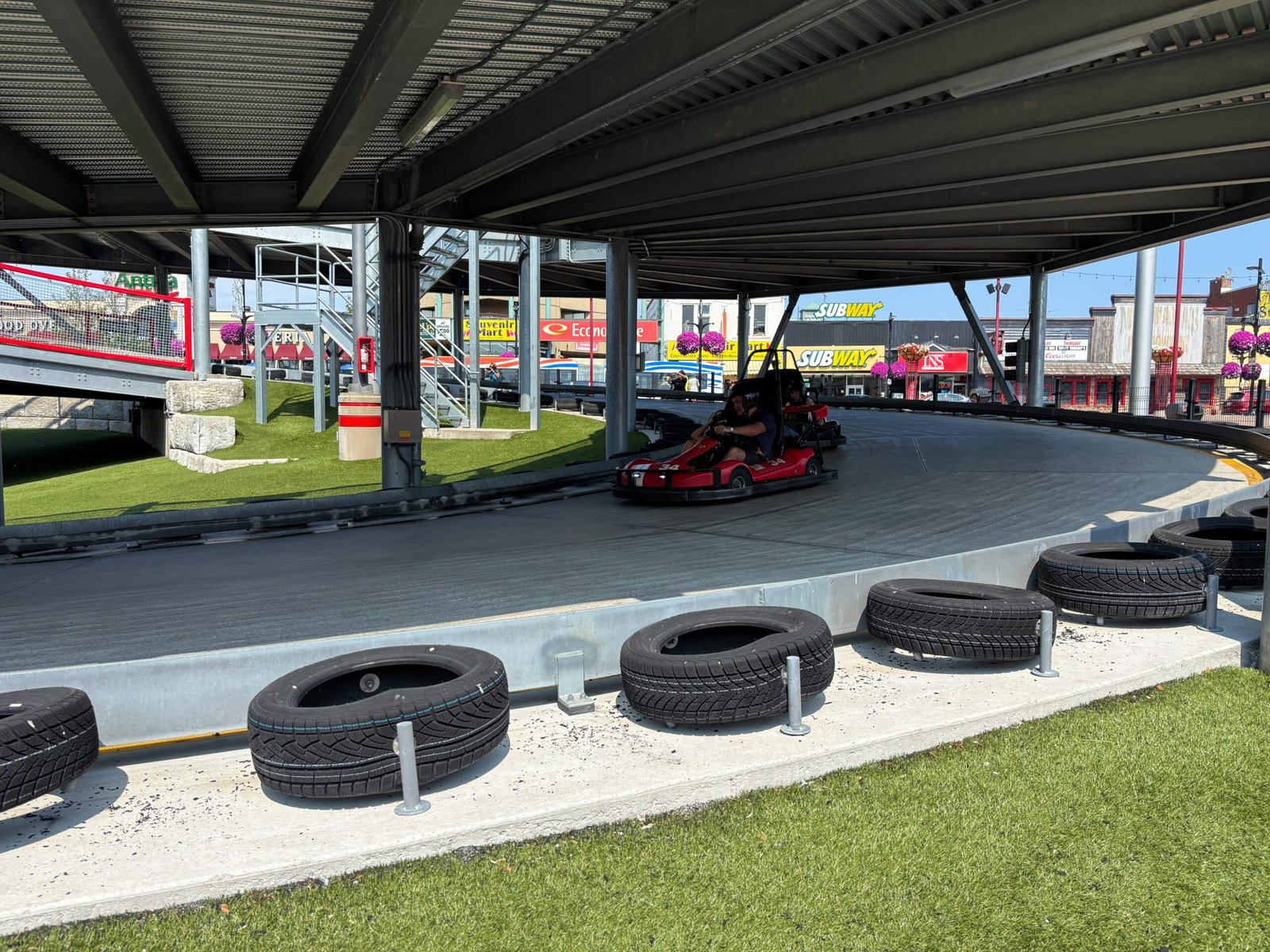 Driver in a red go-kart rounding a curve on the elevated track at Niagara Speedway.
