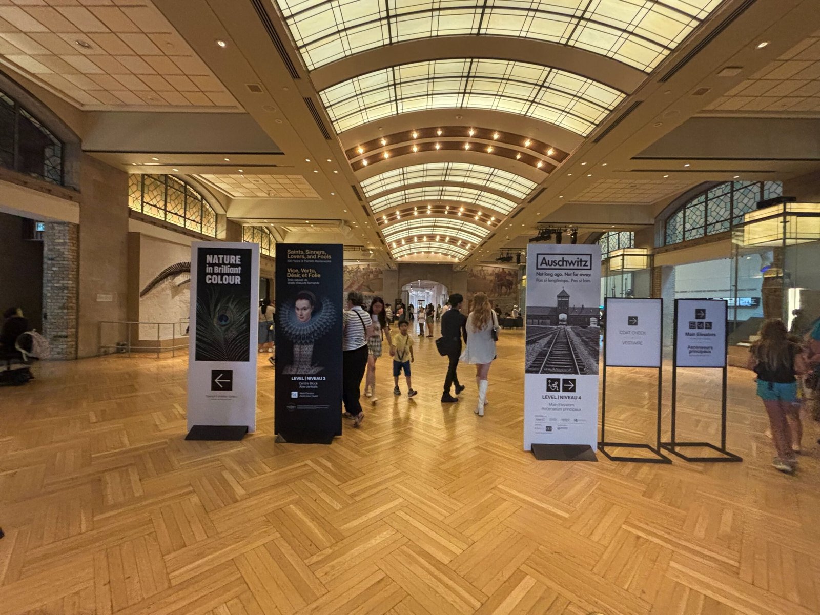 Main lobby of the Royal Ontario Museum with exhibition banners and visitors walking inside.