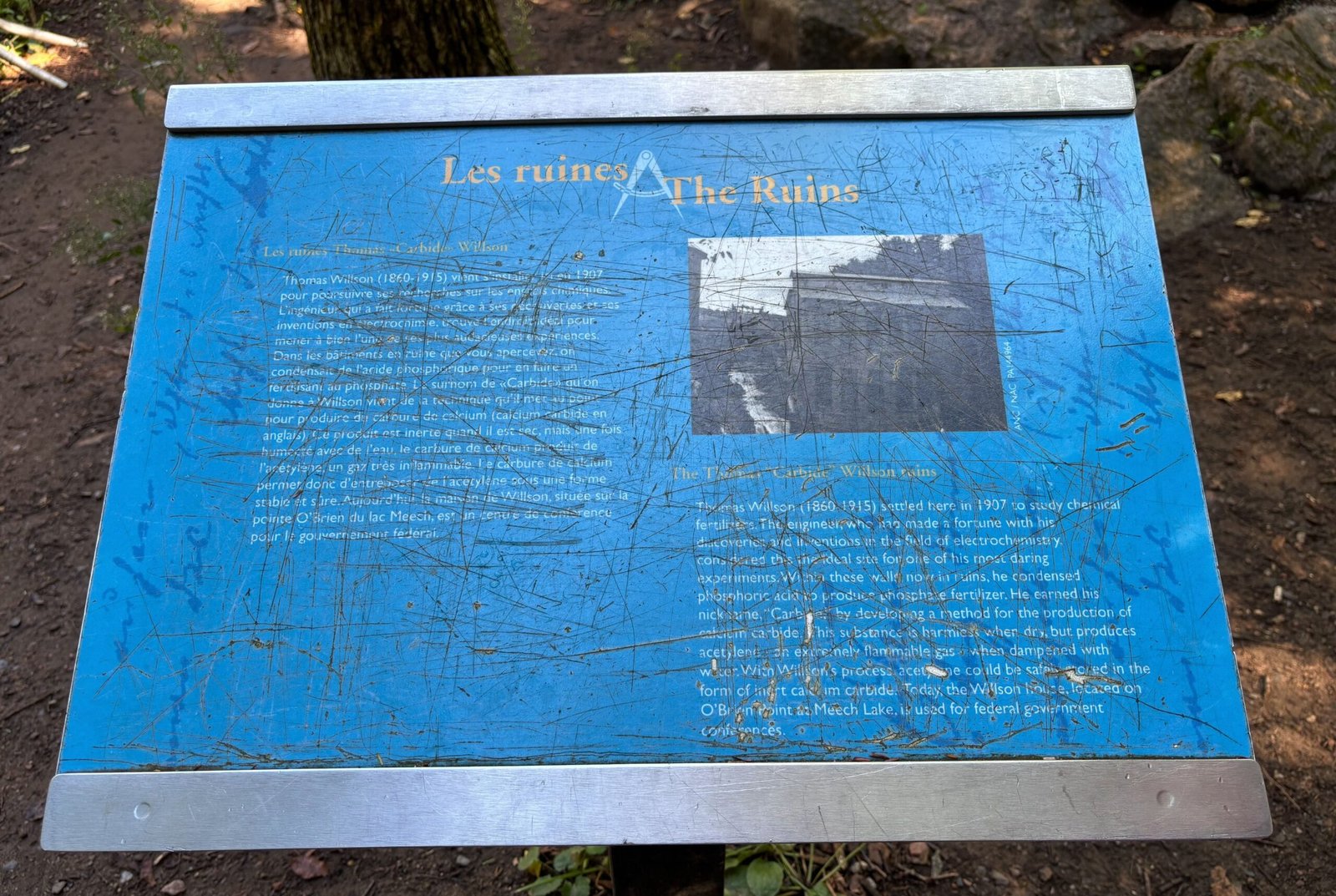 Scratched interpretive sign describing the Carbide Willson Ruins in Gatineau Park, in both French and English