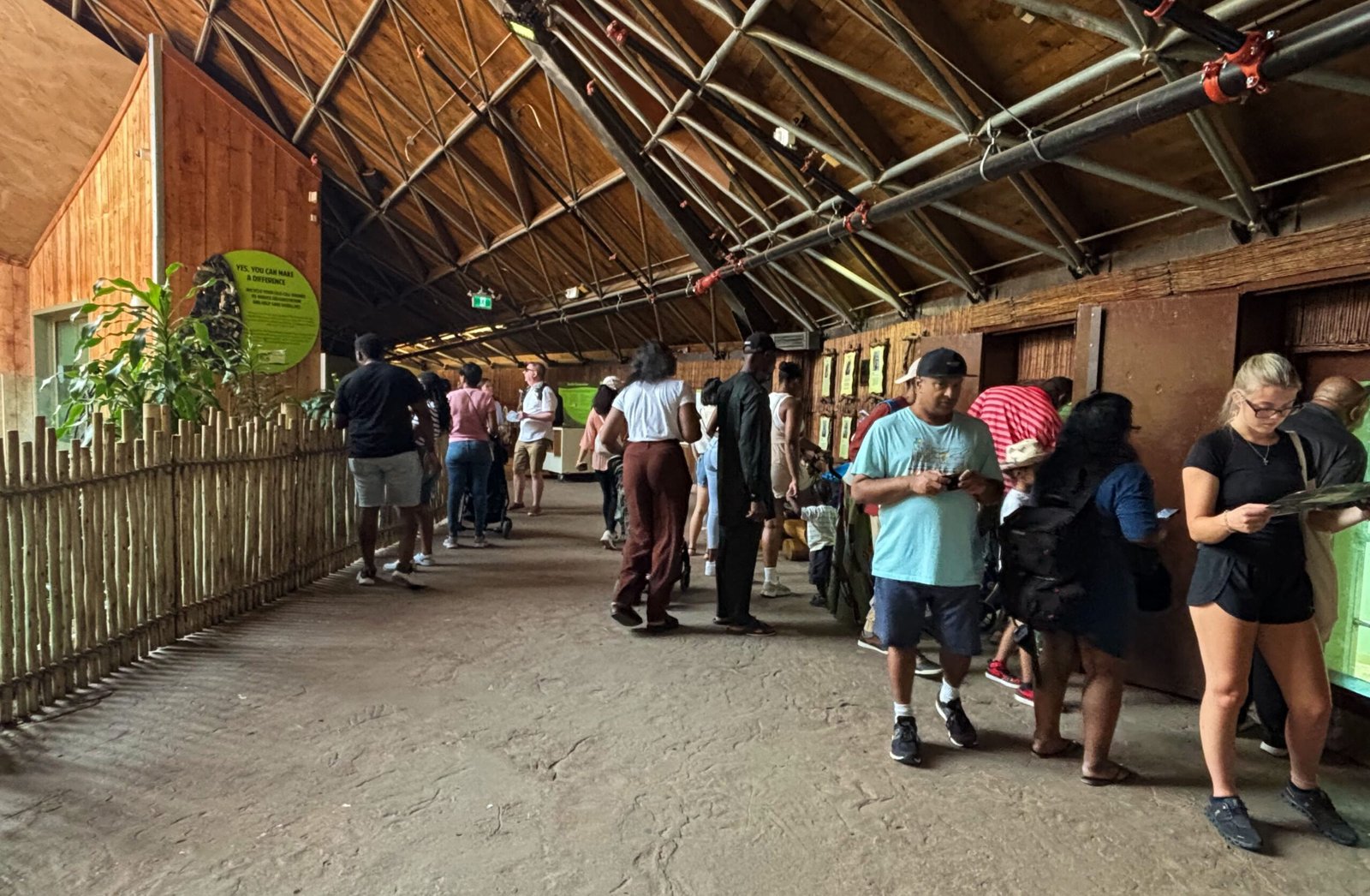 Indoor pavilion with visitors observing animal enclosures along the walls under a thatched-style roof.