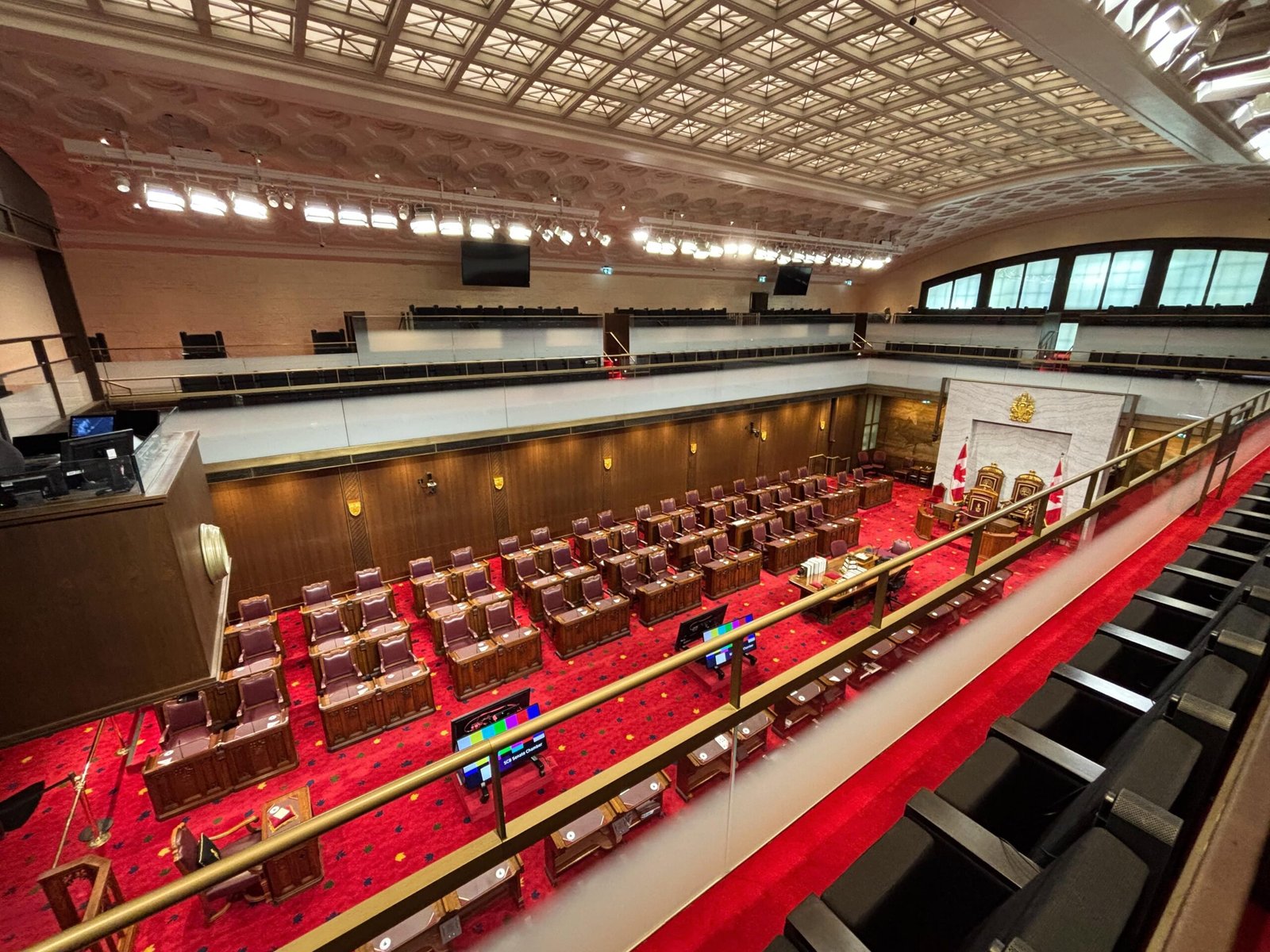 Overhead balcony view of the Senate Chamber with rows of desks and red carpet.