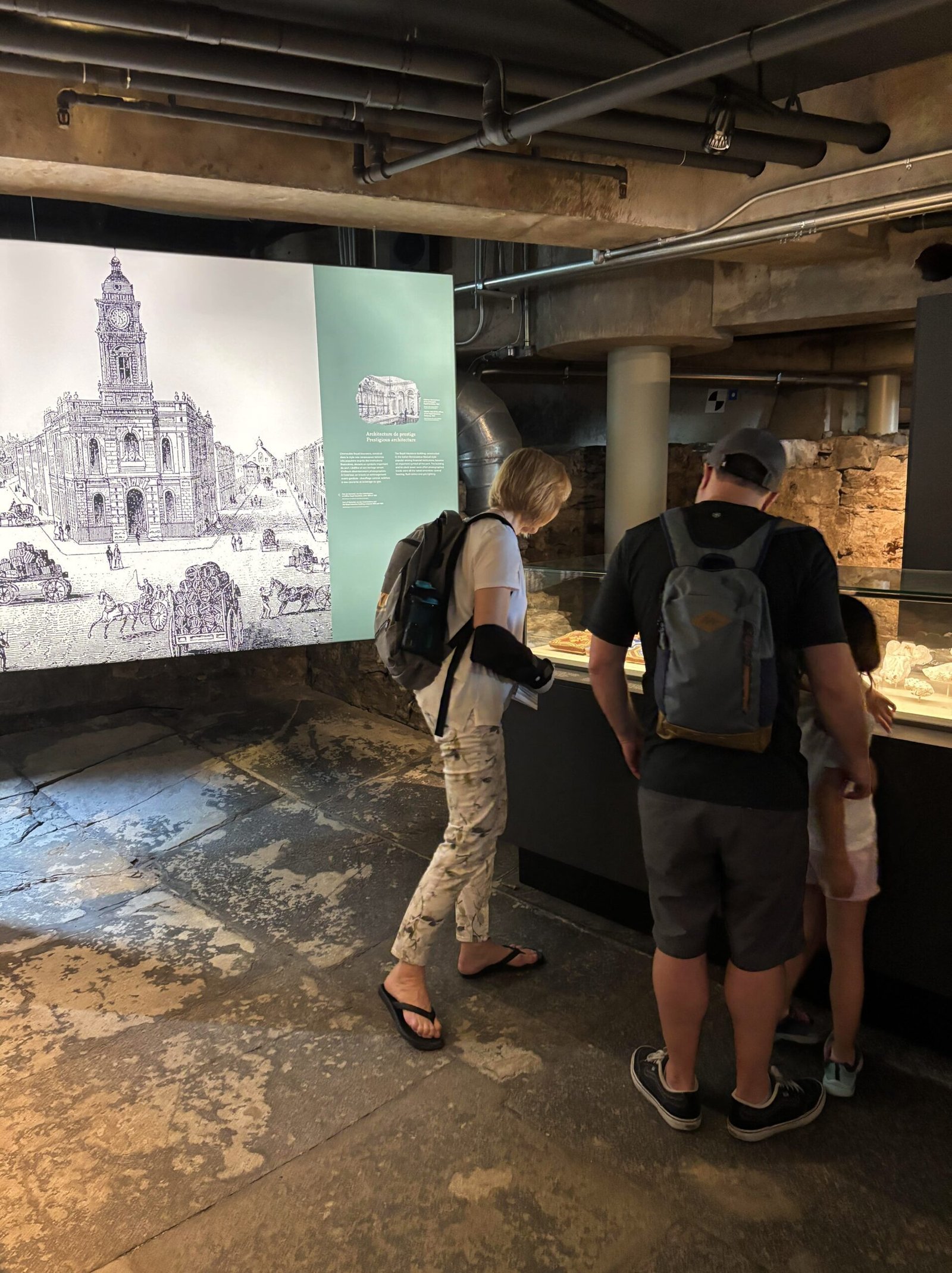 Museum guests viewing ancient objects and stone structures in a dimly lit underground room.
