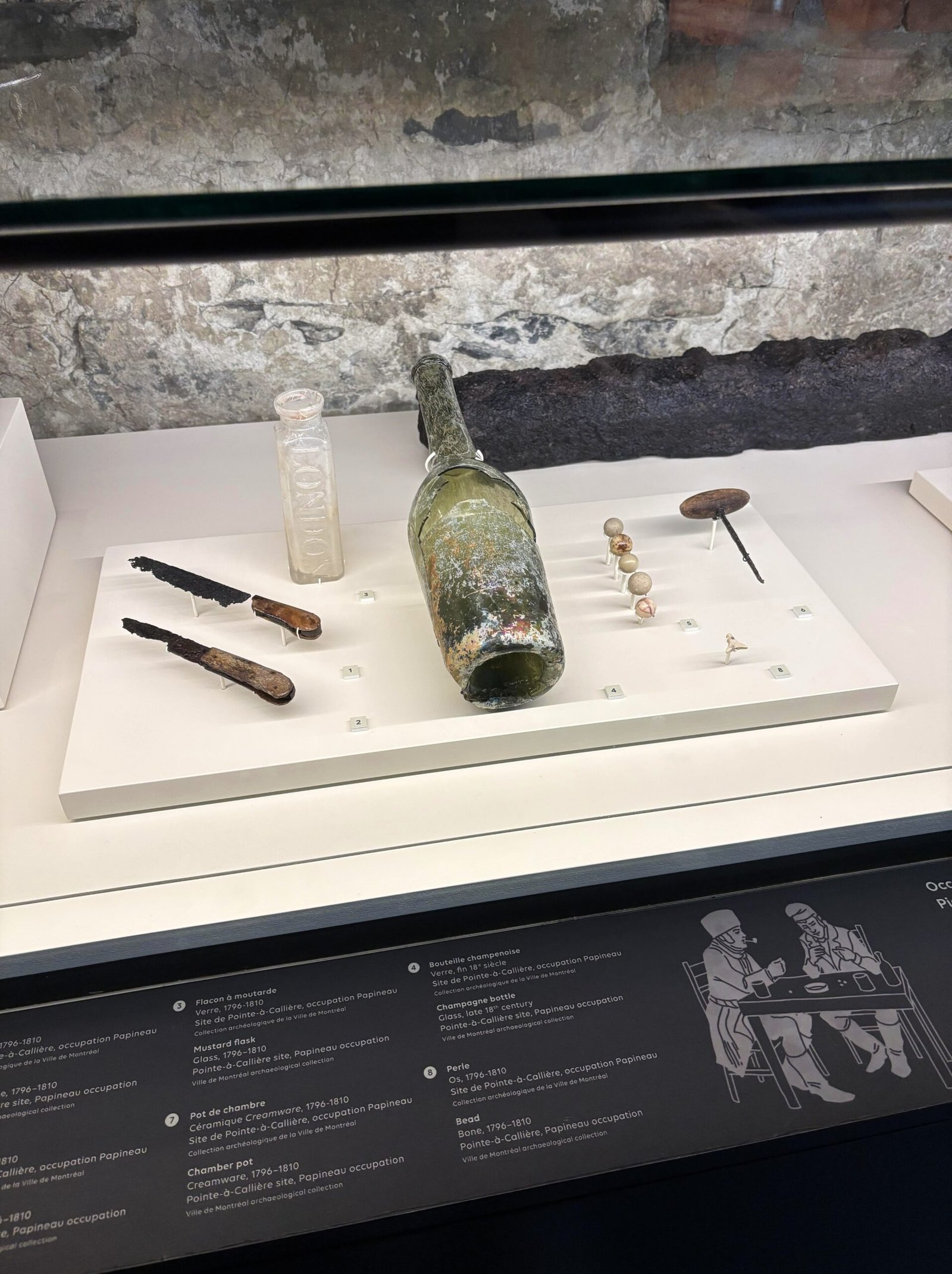 Display case showing old bottles, tools, buttons, and personal items from 1796–1810.