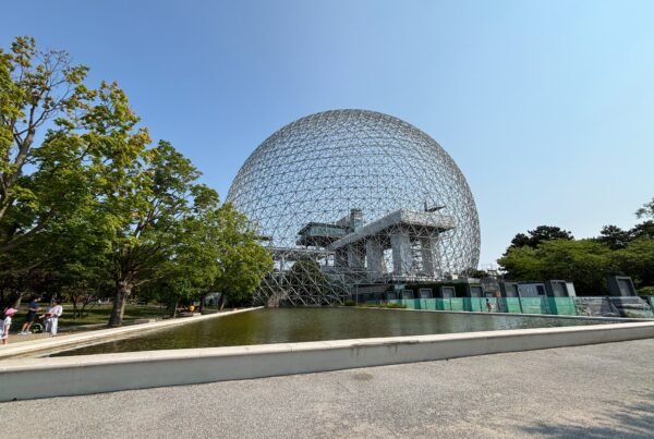 Wide view of Montreal’s Biosphere geodesic dome with reflection pond and trees in foreground.