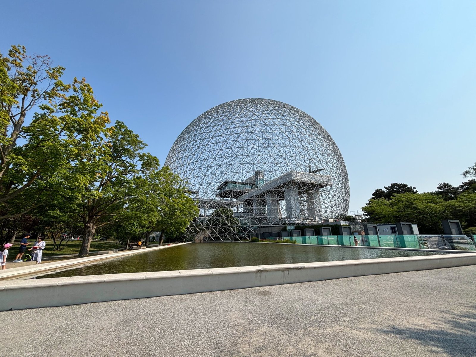 Wide view of Montreal’s Biosphere geodesic dome with reflection pond and trees in foreground.