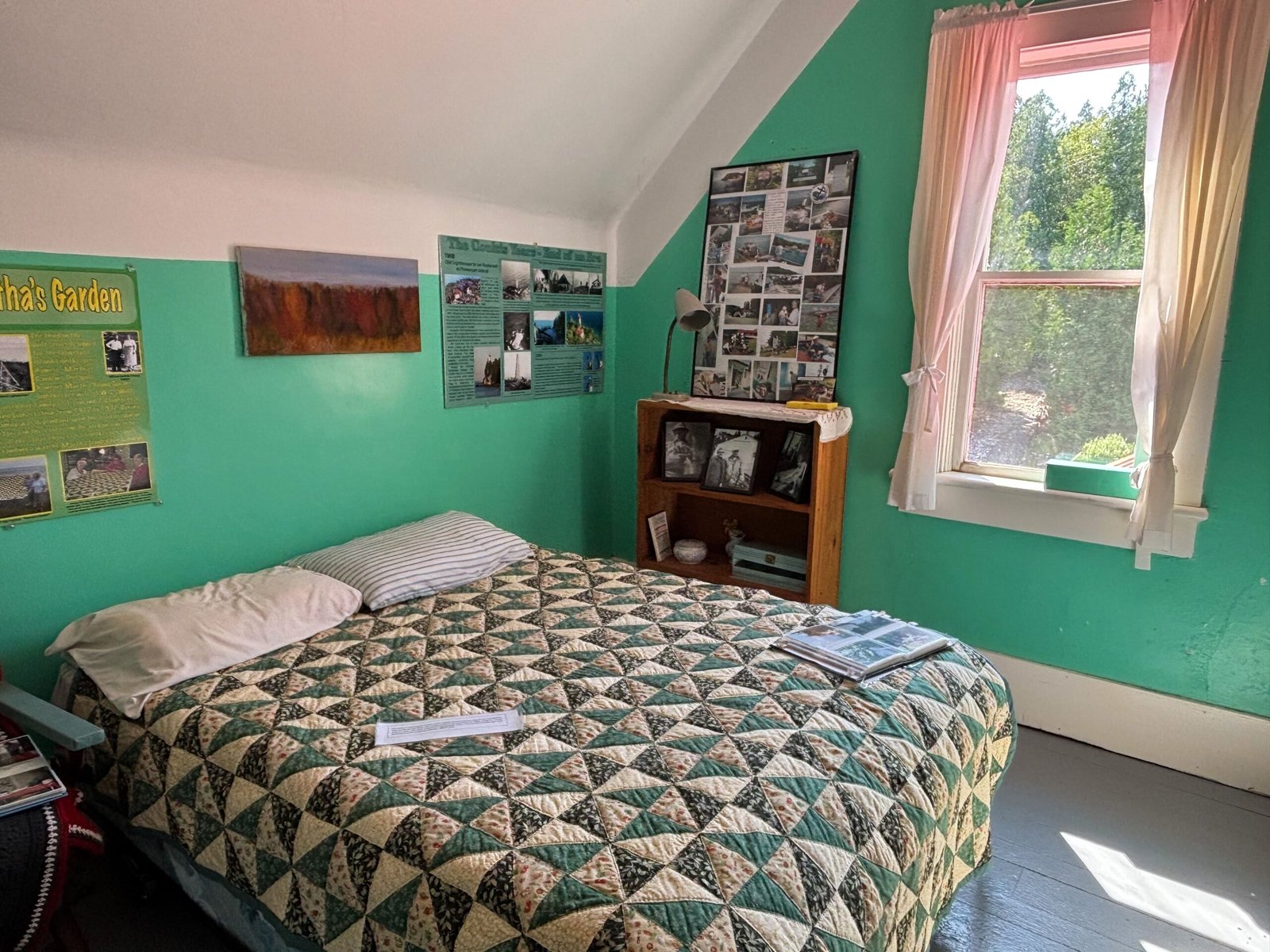 Bedroom with green walls, a patterned quilt on the bed, and photo displays on the walls and shelf.