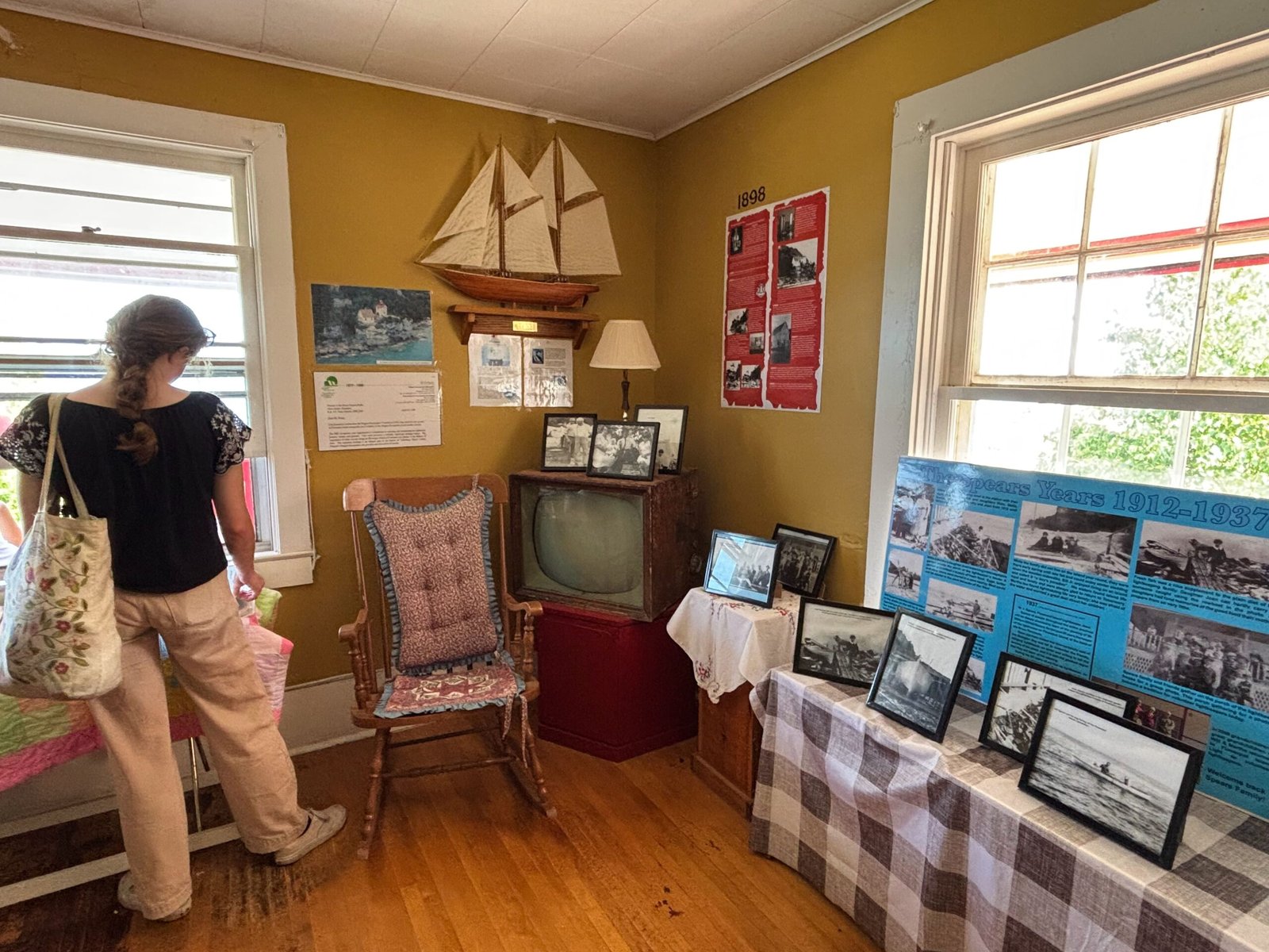 Exhibit room with framed photos, a vintage TV set, a rocking chair, and a model sailboat on the wall.