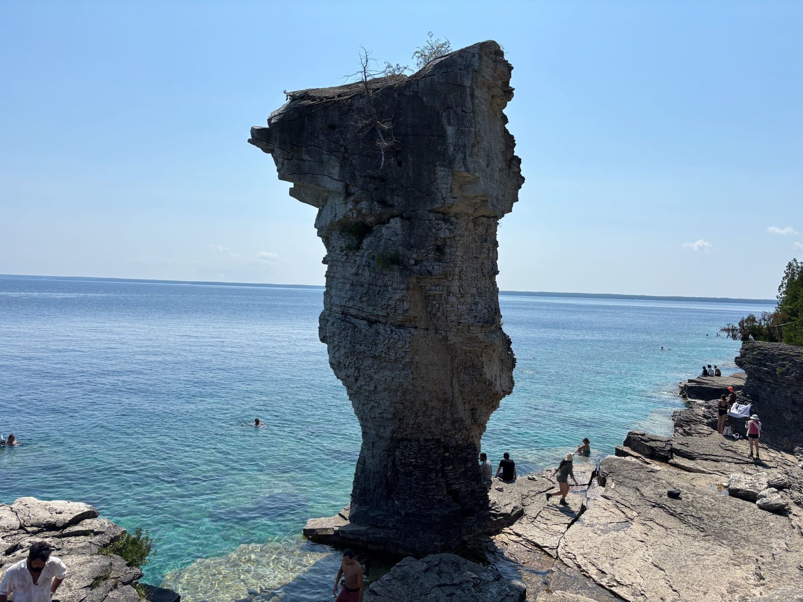 Large stone sea stack known as a Flowerpot rising from clear blue water, with visitors exploring nearby rocks.