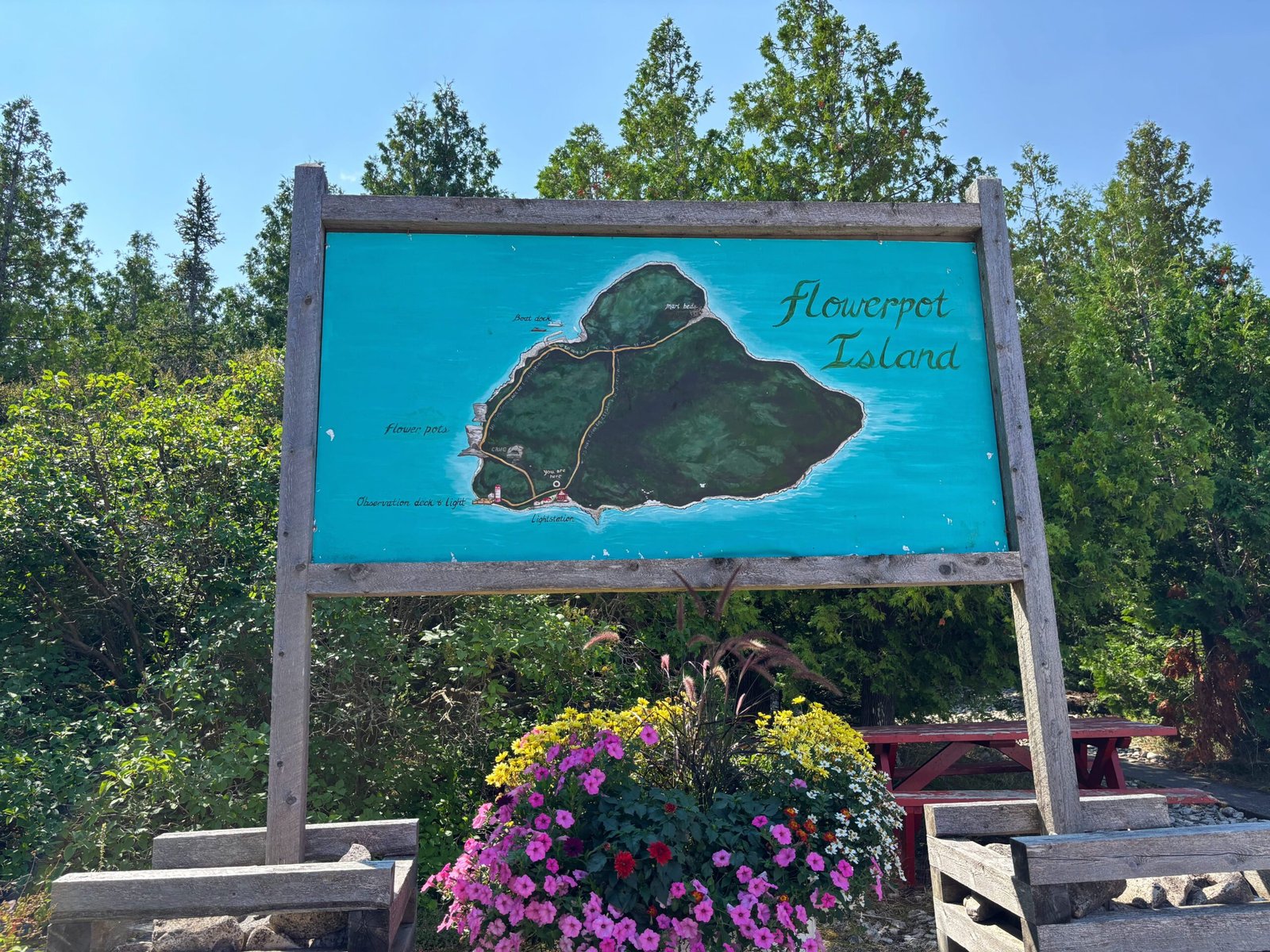 Painted wooden map of Flowerpot Island displayed on a large signboard with flowers below.