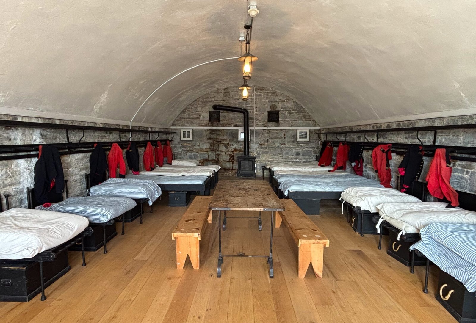 Soldiers’ barracks at Fort Henry with rows of beds, uniforms, and wooden benches.