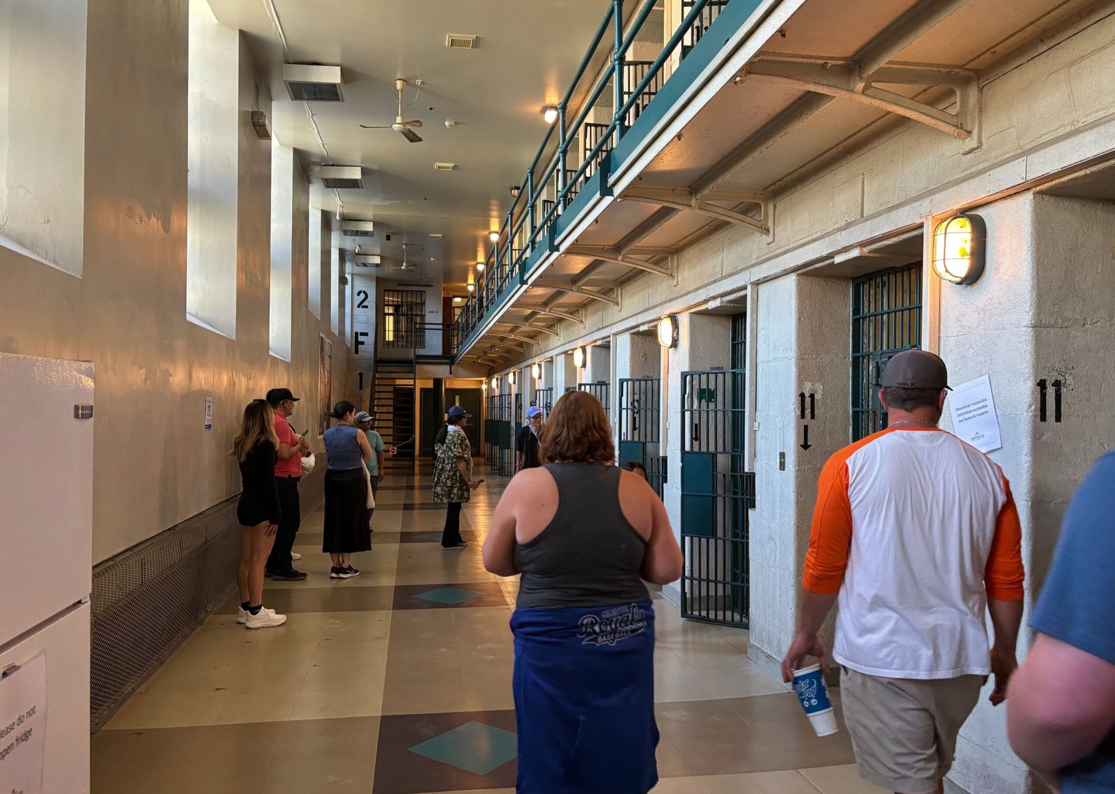 Interior prison cell block with visitors walking past rows of barred doors.