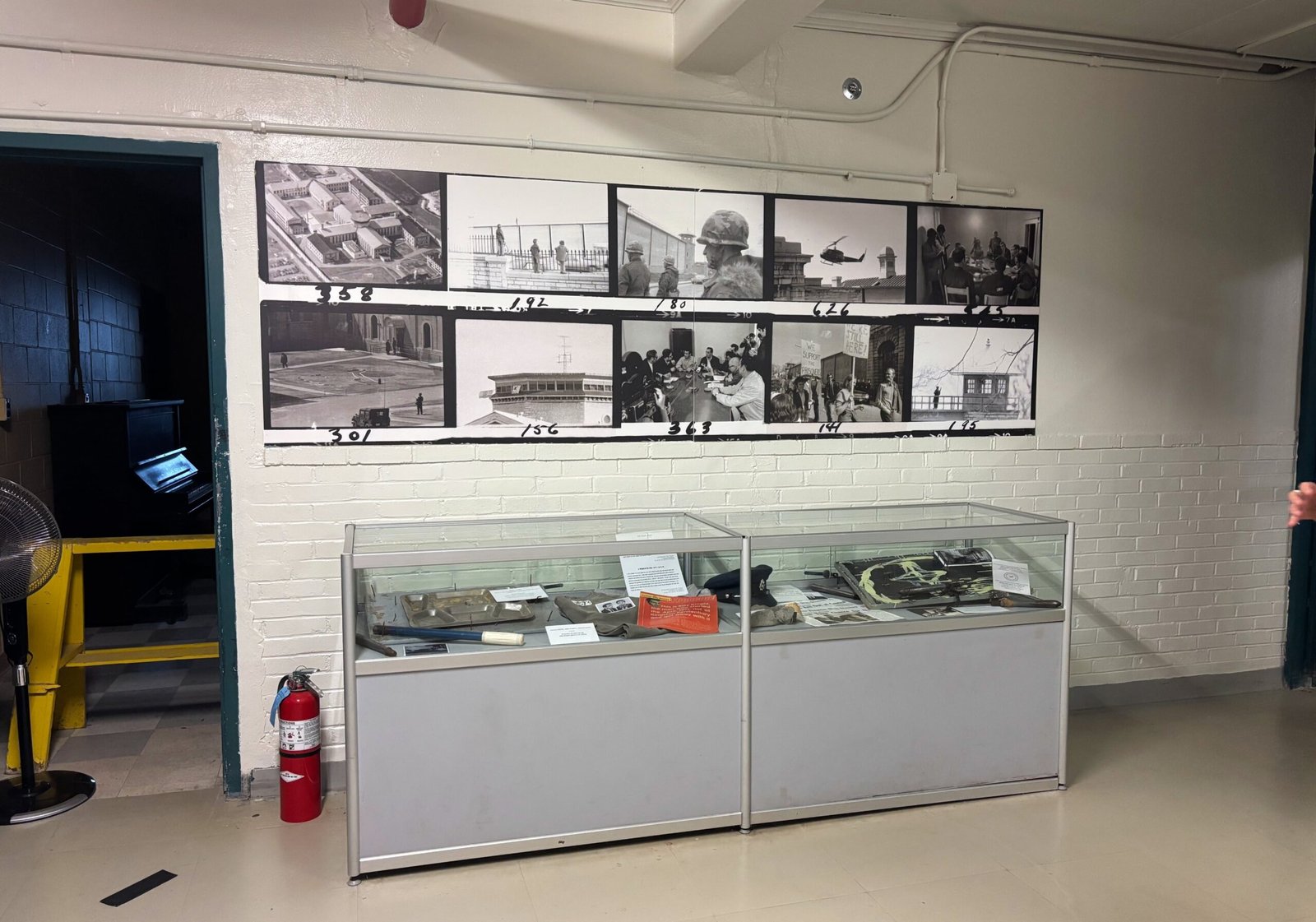 Display case with prison artifacts and historic black-and-white photos on the wall.