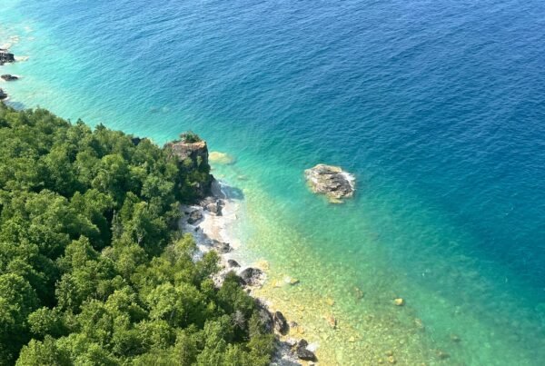 Aerial-style view from the Lion’s Head cliffs showing the forested shoreline, turquoise waters, and rocky outcrops of Georgian Bay.