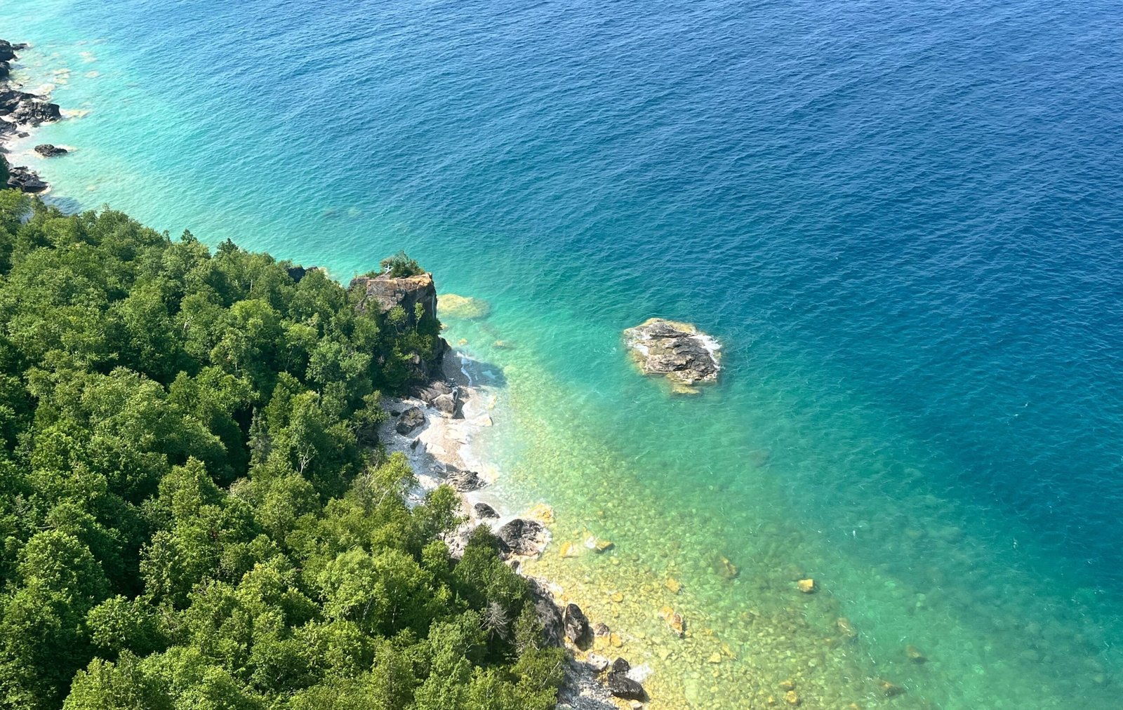 Aerial-style view from the Lion’s Head cliffs showing the forested shoreline, turquoise waters, and rocky outcrops of Georgian Bay.
