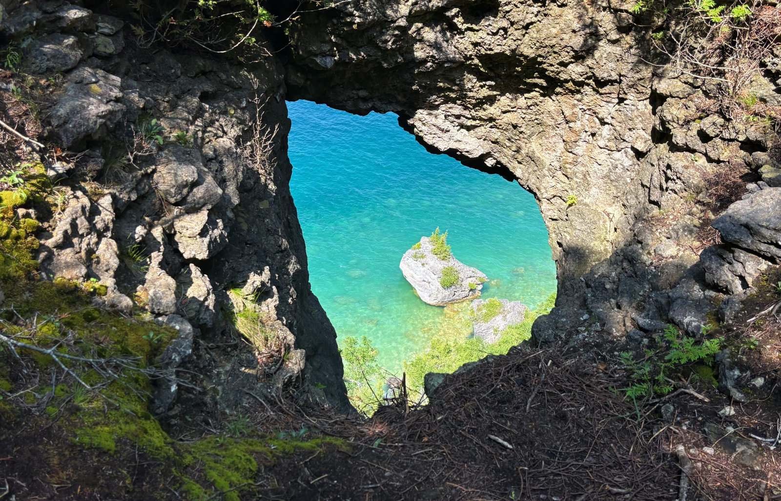 Close-up view through the rocky natural arch at Lion’s Head, with a small rocky island and turquoise bay below.