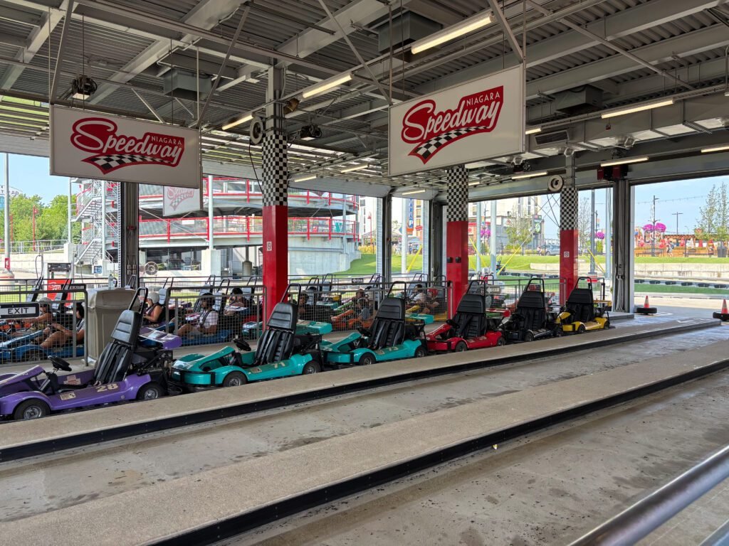 Multiple colorful go-karts parked inside the pit area at Niagara Speedway, with the elevated track visible outside.