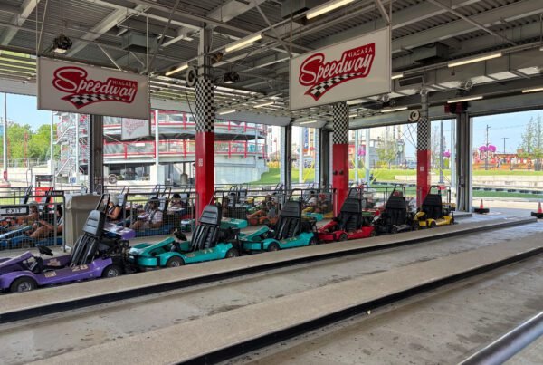 Multiple colorful go-karts parked inside the pit area at Niagara Speedway, with the elevated track visible outside.