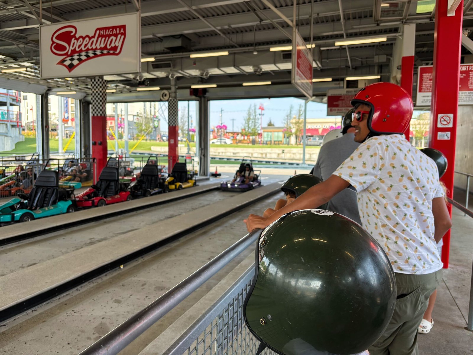 Visitor wearing a helmet waiting in line near the track at Niagara Speedway, with go-karts parked in the background.