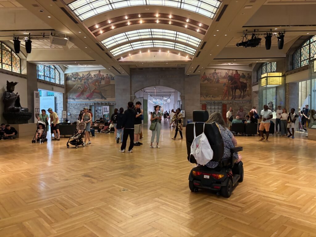 Visitors in the main gallery hall of the Royal Ontario Museum with murals and wooden floors.