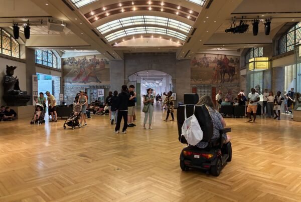 Visitors in the main gallery hall of the Royal Ontario Museum with murals and wooden floors.