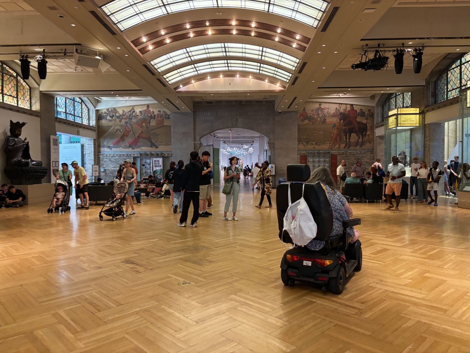 Visitors in the main gallery hall of the Royal Ontario Museum with murals and wooden floors.