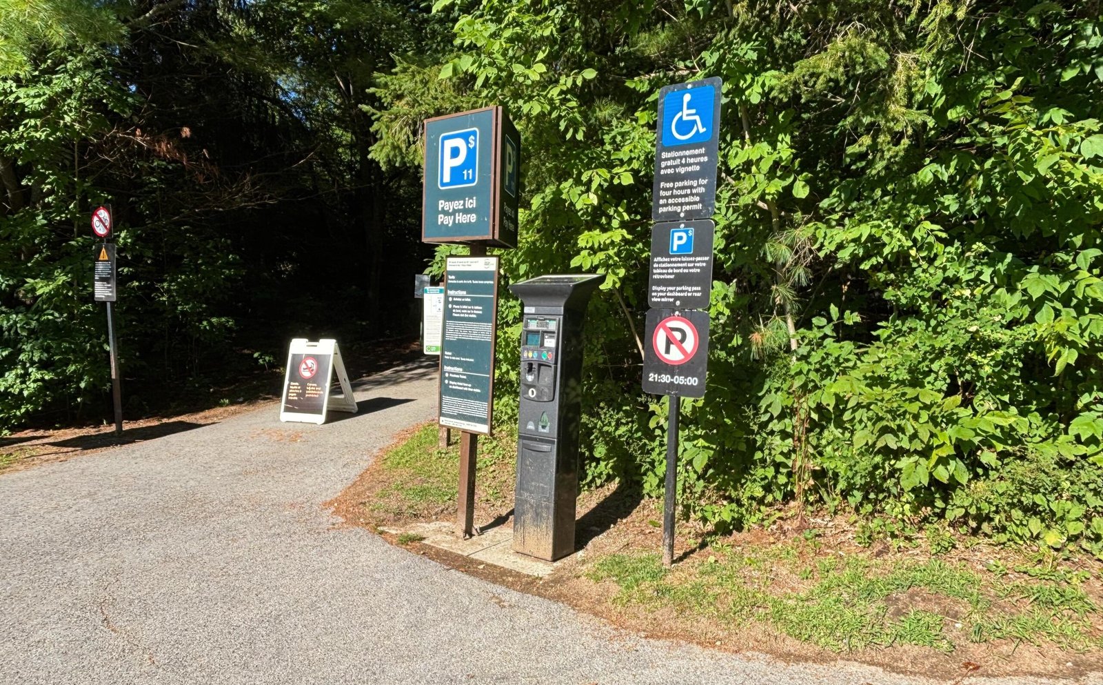 Parking pay station and information signs at the entrance to Carbide Willson Ruins trail in Gatineau Park.