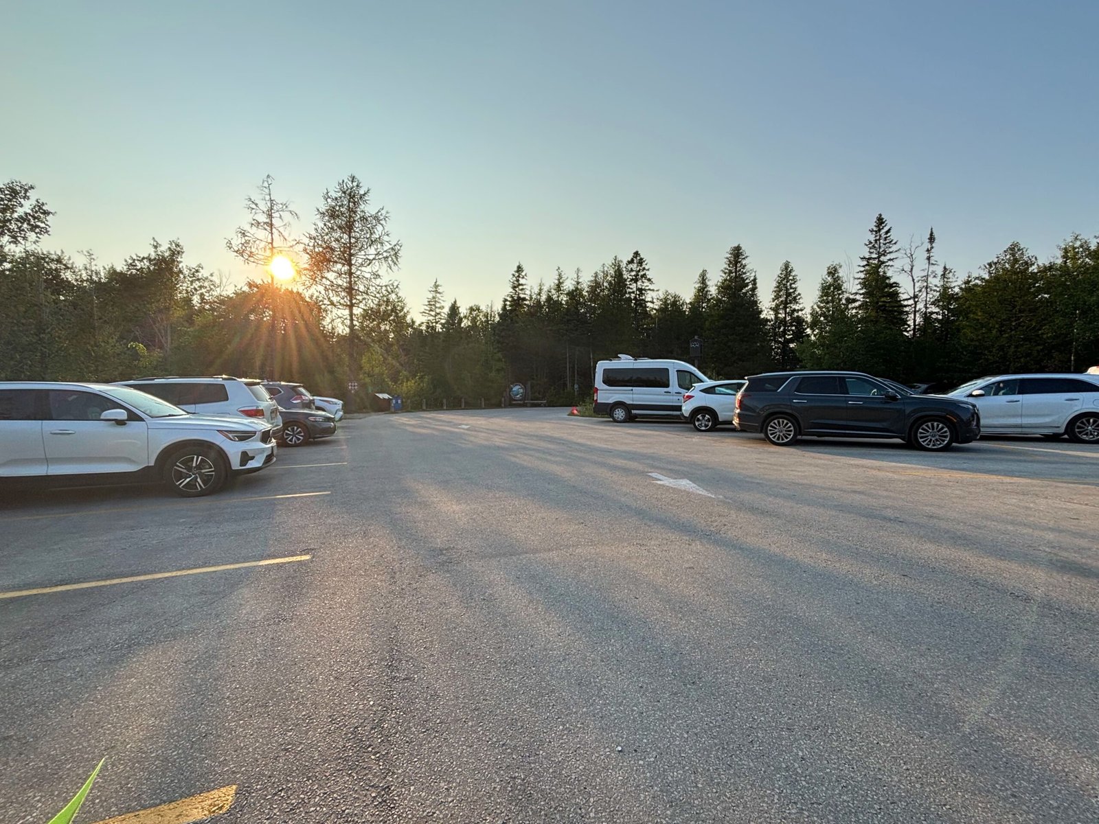 Cars parked in the Bruce Peninsula National Park parking lot with the sun setting over the trees in the background.