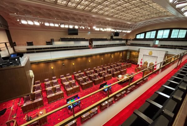 Overhead balcony view of the Senate Chamber with rows of desks and red carpet.
